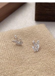 Detail of silver S925 butterfly stud earrings with brushed texture on knit background