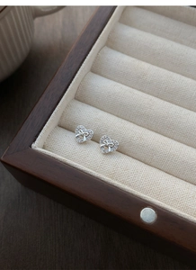Close-up of S999 silver hollow bow heart earrings with pavé crystals in a wooden box