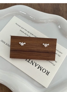 Macro detail of silver stud earrings with three sparkling zircons on wooden display stand