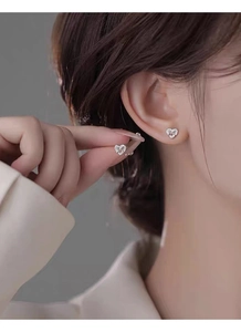 Detailed view of sterling silver hollow heart studs with crystals on model's ear