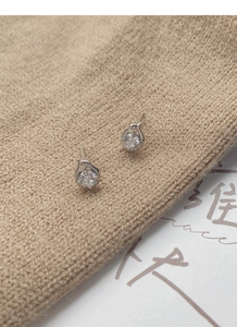 Macro shot of silver snake-shaped earrings with large round zircon studs on a warm fabric