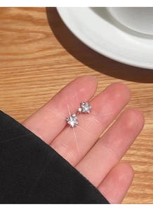 Détail de boucles d'oreilles étoile en argent avec cristaux tenues à la main sur bois