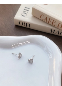 Macro shot of silver heart studs with floral cut-out and pave stones on porcelain