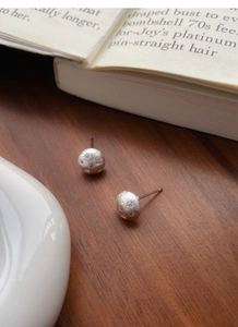 Macro detail of S925 sterling silver brushed starburst earrings on a vintage wooden desk