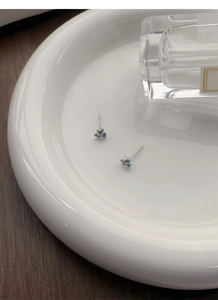 Détail de boucles d'oreilles iris bleus en argent S999 sur plateau en céramique