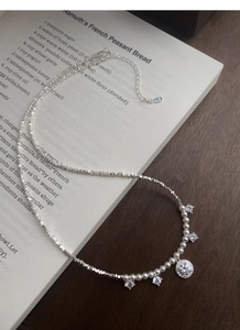 Détail du collier en argent S925 avec perles et breloques en zircon sur un livre