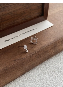 Macro detail of asymmetric silver cat and fishbone stud earrings with pavé zircon stones