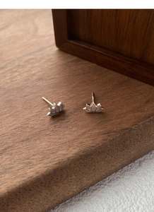 Macro shot of S999 sterling silver lotus stud earrings on a dark walnut wooden surface