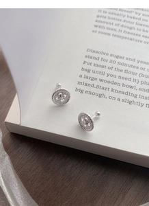 Detailed view of S999 sterling silver button stud earrings on an open book