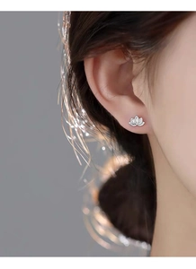 Detailed view of S999 silver lotus stud earrings worn on ear with soft bokeh background