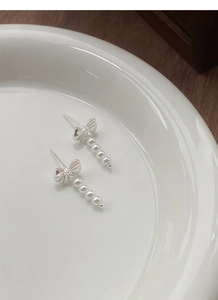 Detailed macro view of S925 silver bow stud earrings with white pearl tassels on ceramic