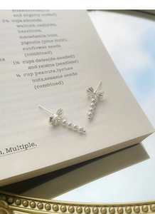 Detailed view of silver bowknot pearl tassel earrings on an aesthetic vintage book background