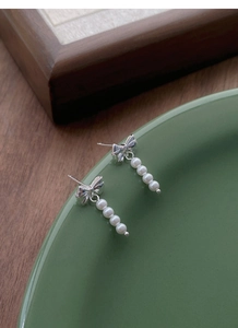 Close-up of silver bow earrings with four drop pearls on a green ceramic tray