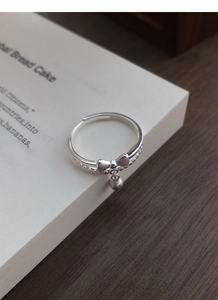 Detail of S925 silver double layer ring with frosted bow and bell charm on a book
