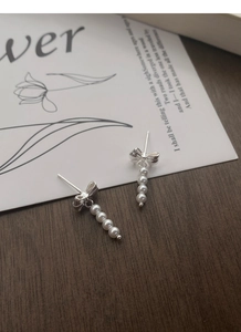 Macro detail of S925 silver bow stud earrings with delicate dangling faux pearls