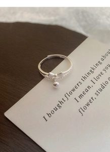 Detail of S925 sterling silver bow ring with round bead charm on a wooden background