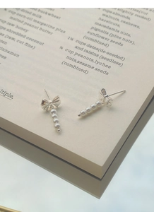 Macro shot of S925 silver bow earrings with five dangling white pearls on a magazine