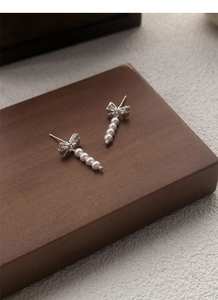Detail of silver bow earrings with four vertical pearls on a dark wooden display