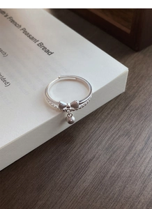Detailed macro view of S925 sterling silver bow ring with bead drop on a white book surface
