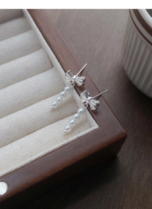 Detail of silver bow earrings featuring five cascading white pearls on soft velvet