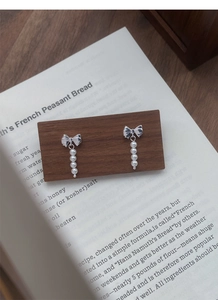 Detail of silver bow earrings with four vertical pearls on a vintage wooden background