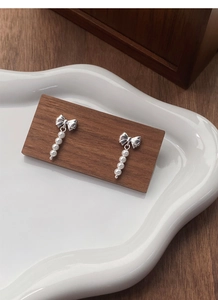 Detail of silver bow stud earrings with dangling white pearl tassels on ceramic tray