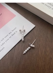 Detail of S925 silver bow stud earrings with graduated white pearl tassels on wood