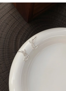 Detail of silver hollow rabbit stud earrings with shiny zircon on white ceramic tray