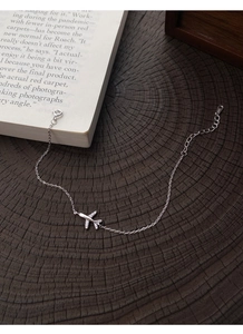 Detail of S999 silver airplane bracelet featuring micro-paved wings on dark wood background