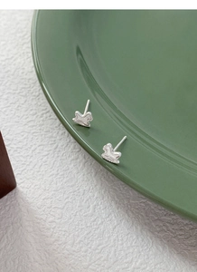 Close-up of S999 silver horse stud earrings with a matte texture on a ceramic dish