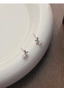 Close-up of S999 sterling silver cherry pearl stud earrings on a white ceramic plate