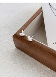 Detailed view of tiny silver rocking horse stud earrings on a minimalist wooden tray