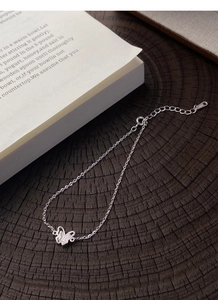 Dettaglio del bracciale con farfalla in argento S999 su sfondo rustico in legno