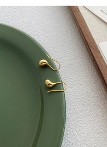 Orecchini a goccia dorati lucidi appesi sul bordo di un piatto in ceramica verde