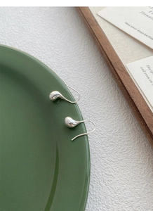 Dettaglio macro di orecchini a goccia in argento su un vassoio verde dal design moderno