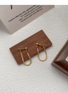 Macro shot of gold S925 silver stud earrings with cascading fine chain on wood block
