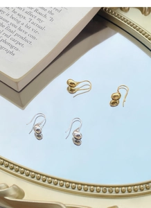 Dettaglio di orecchini a goccia in argento e oro riflessi su uno specchio vintage
