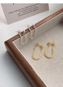 Close-up of S925 sterling silver and gold U-shaped drop chain earrings on a linen tray