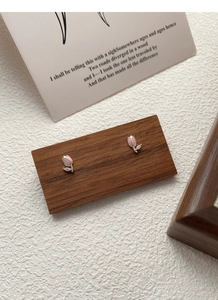 Makro-Detail von Tulpen-Ohrsteckern mit rosa Glasur und Zirkonia auf einem Holzsockel
