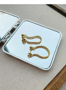 Macro shot of gold spherical stud earrings with textured star chain on mirror