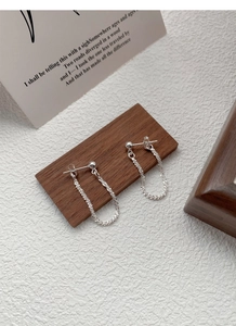 Close-up of S925 sterling silver drop chain earrings on wooden display with card