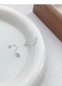Macro detail of S999 silver teardrop screw-back earrings on minimalist white ceramic plate