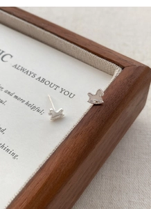 Close-up of minimalist S999 silver rocking horse stud earrings on a fabric display