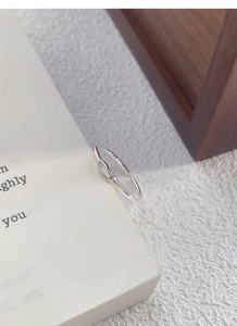 Detail view of a minimalist S999 silver fish ring on a white book with soft lighting