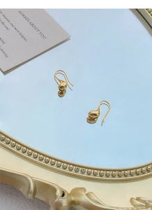 Dettaglio di eleganti orecchini a goccia dorati su uno specchio vintage con riflessi