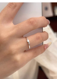 Macro detail of a minimalist S999 sterling silver fish ring worn on a person hand