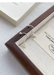 Macro detail of silver drop earrings with screw back on a wooden jewelry tray