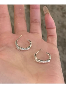 Detailed view of silver C-shaped bow earrings with textured surface held in hand