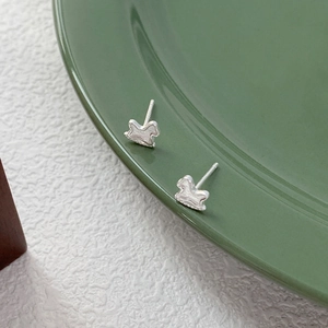 Minimalist S999 sterling silver rocking horse stud earrings on a green ceramic plate