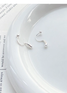 Macro shot of silver teardrop earrings on white ceramic dish with sleek polished finish